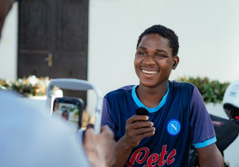 Un jeune est tient un micro en étant interviewé et filmé par l'équipe ZOA